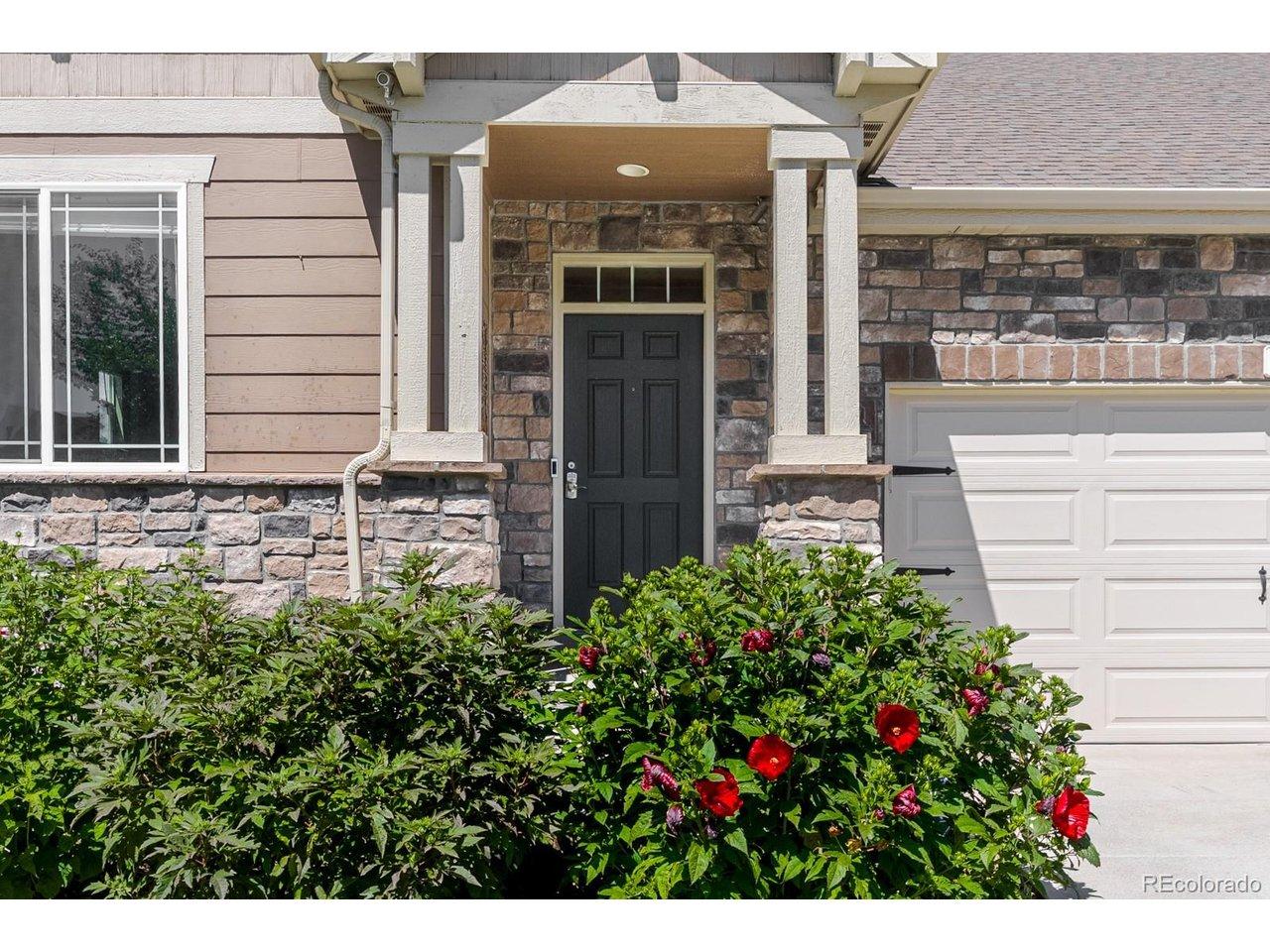 Image 2: Lush landscaping frames the inviting exterior, while vibrant blooming hibiscus plants-well known throughout the neighborhood-create a colorful welcome that returns year after year.