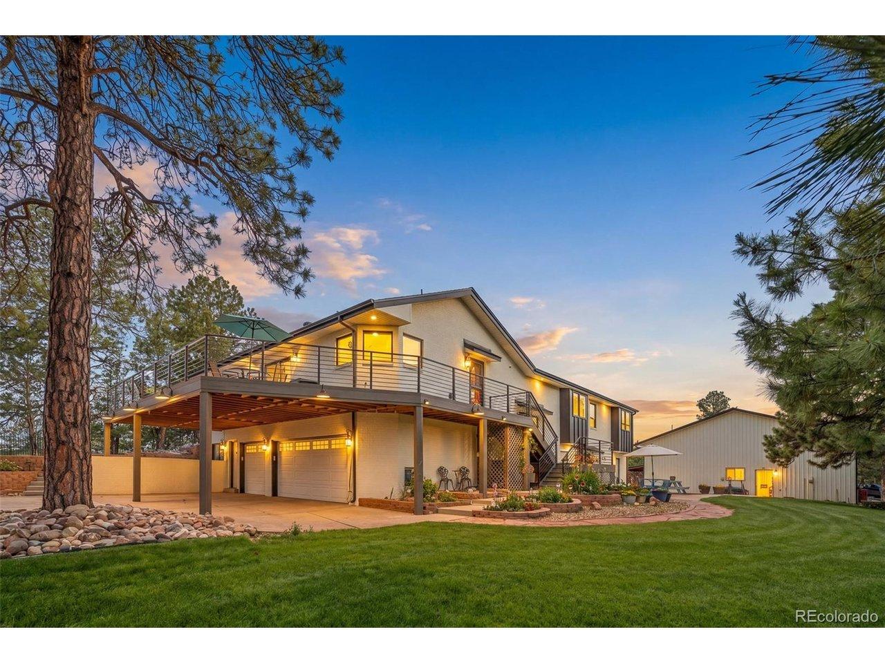 Image 3: Exterior view of the home, expansive wraparound deck, manicured lawn, 3-car garage, and detached shop, all surrounded by mature trees and evening light. Image 3: Exterior view of the home, expansive wraparound deck, manicured lawn, 3-car garage, and detached shop, all surrounded by mature trees and evening light.