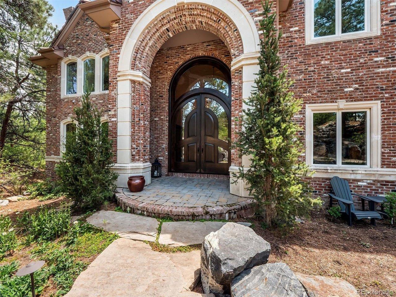 Image 2: Elegant exterior entry with custom arched door, rich brick detail, set just beyond the water feature