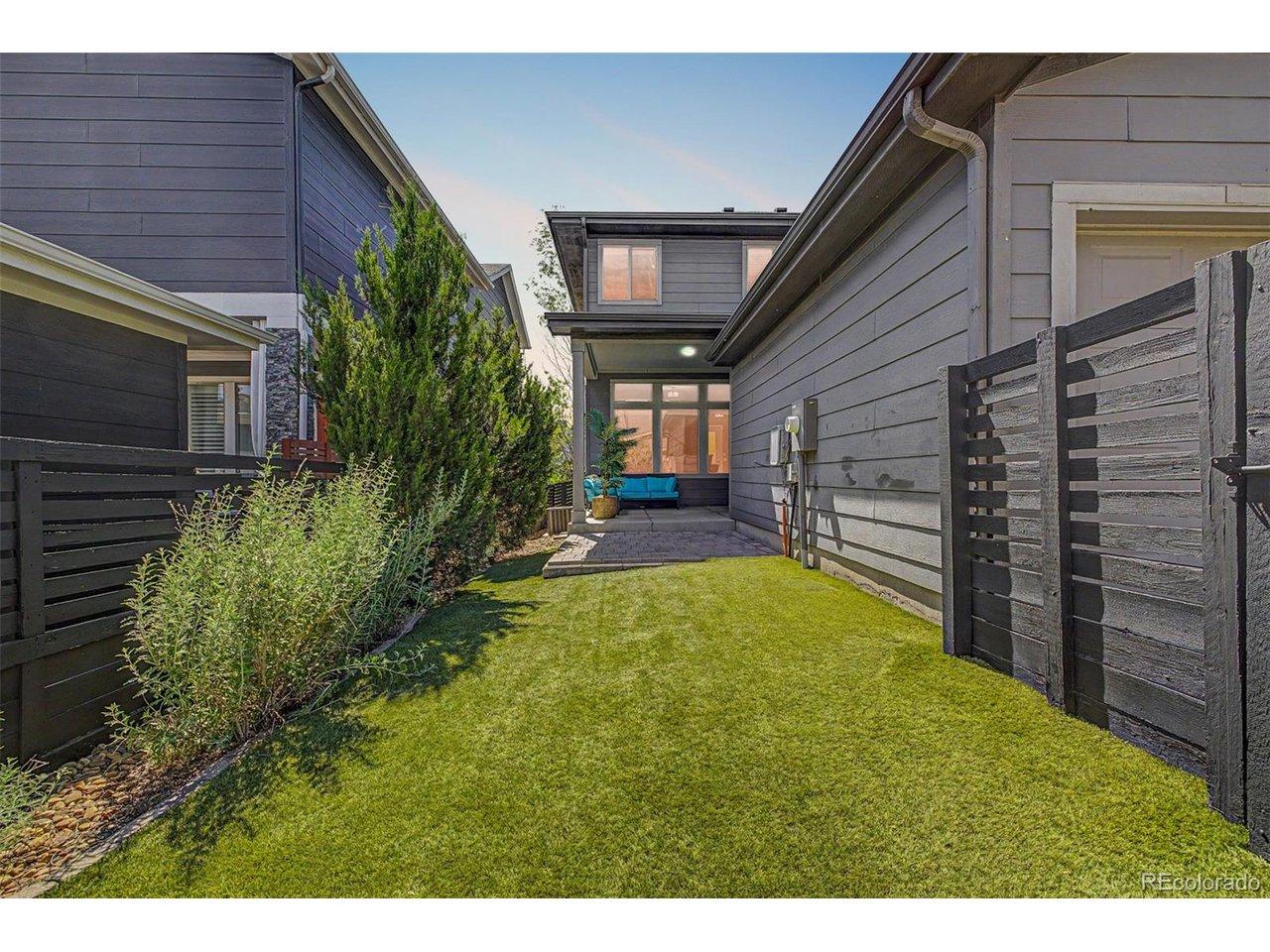 Image 2: Backyard preview: Enchanting evening view of the private fenced backyard featuring lush turf lawn, mature evergreen landscaping, paver walkway, covered patio with outdoor seating, and warm interior lights glowing through the large windows - the perfect out Image 2: Backyard preview: Enchanting evening view of the private fenced backyard featuring lush turf lawn, mature evergreen landscaping, paver walkway, covered patio with outdoor seating, and warm interior lights glowing through the large windows - the perfect out