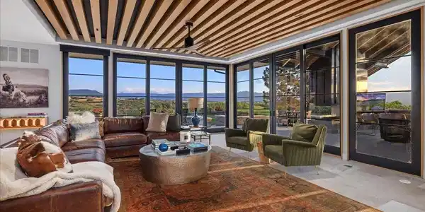 Image 4: The stunning Great Room showcases soaring ceilings with custom white oak beams, walls of glass, and panoramic mountain views that blur the line between indoors and out. Image 4: The stunning Great Room showcases soaring ceilings with custom white oak beams, walls of glass, and panoramic mountain views that blur the line between indoors and out.