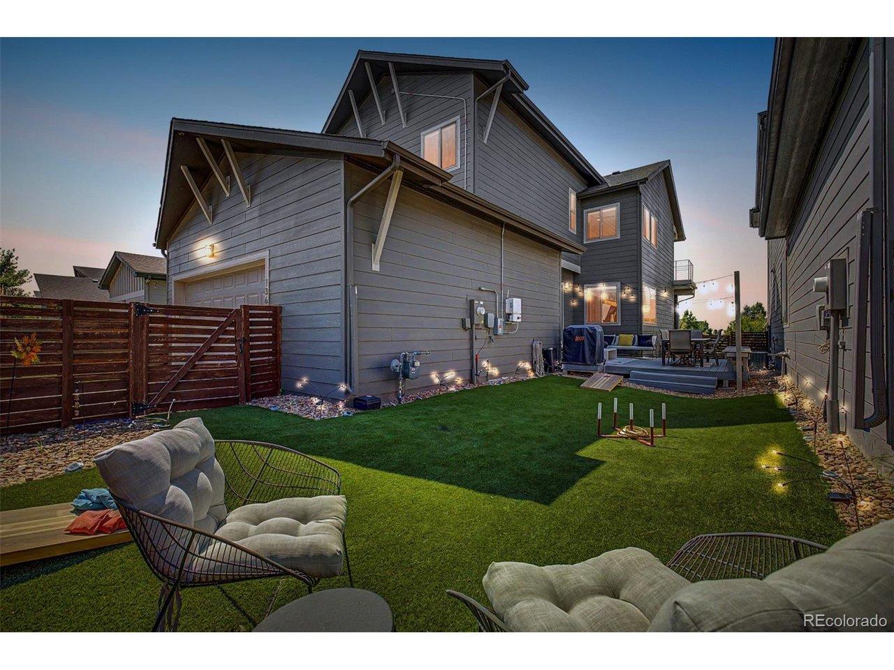 Image 3: Magical twilight view of the fully fenced backyard showcasing lush artificial turf, landscape lighting, lawn game area, and a beautifully lit composite deck with string lights and outdoor dining. The detached garage, upper balcony, and glowing interior win Image 3: Magical twilight view of the fully fenced backyard showcasing lush artificial turf, landscape lighting, lawn game area, and a beautifully lit composite deck with string lights and outdoor dining. The detached garage, upper balcony, and glowing interior win