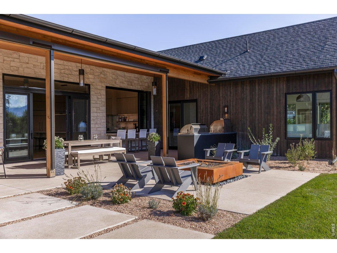 Image 2: Designed for seamless outdoor living, the west patio showcases panoramic mountain scenery with multiple seating areas, a fire pit, and a fully equipped summer kitchen-complete with pizza oven, grill, and beverage fridge.