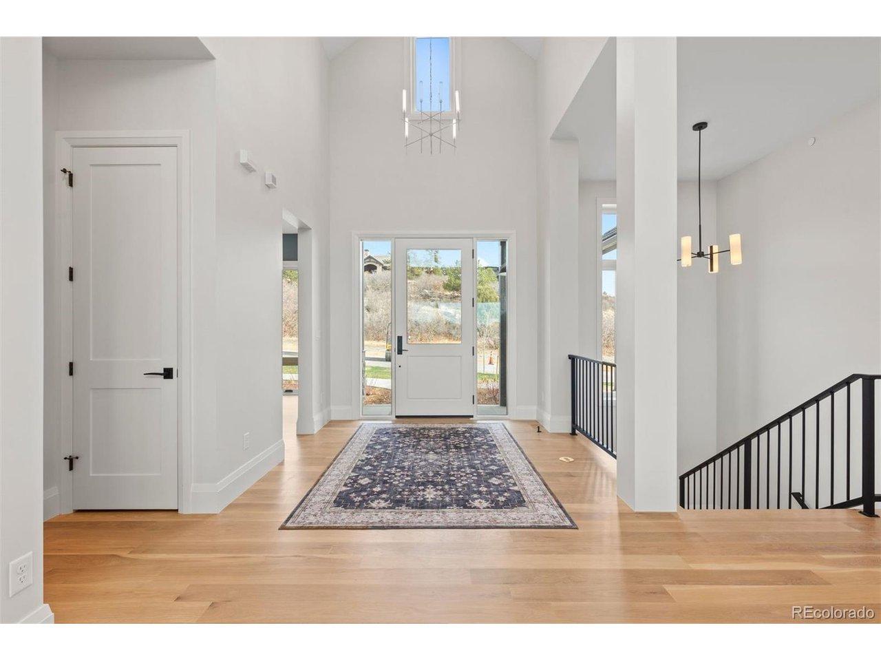 Image 3: A soaring, light-filled foyer defined by clean architectural lines, dramatic ceiling height, and a striking vertical window that draws the eye upward.