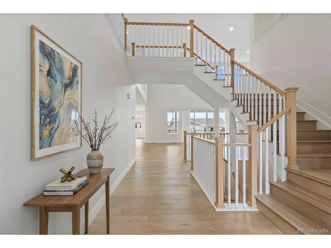Image 3: A grand, light-filled foyer showcases soaring ceilings, warm wood floors, and an elegant staircase that sets a refined tone for the home. *This photo has been virtually staged. Image 3: A grand, light-filled foyer showcases soaring ceilings, warm wood floors, and an elegant staircase that sets a refined tone for the home. *This photo has been virtually staged.