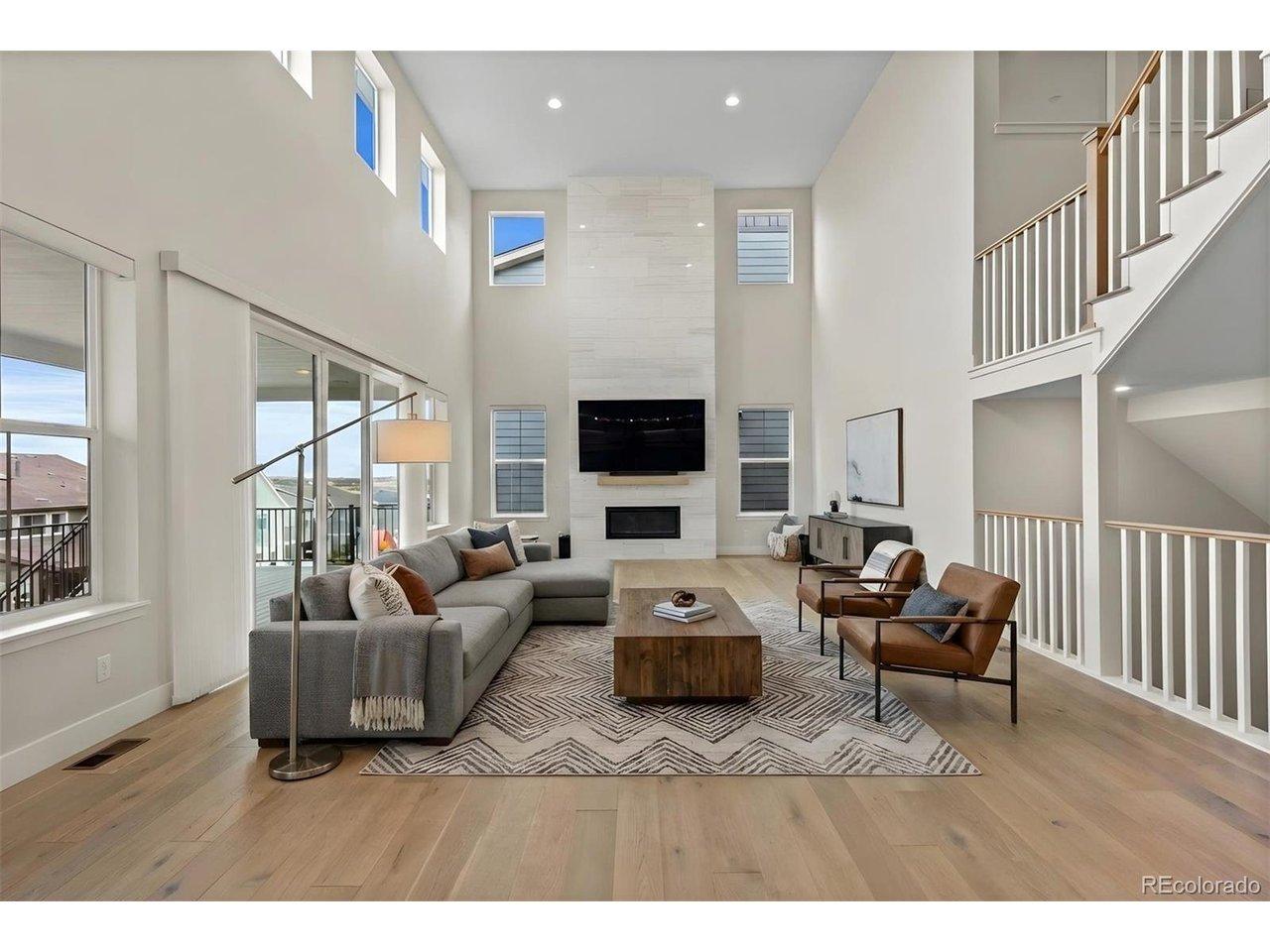 Image 4: Bathed in natural light from soaring windows, the great room impresses with dramatic ceiling heights, a sleek fireplace focal point, and seamless access to the covered deck for elevated indoor-outdoor living. *This photo has been virtually staged. Image 4: Bathed in natural light from soaring windows, the great room impresses with dramatic ceiling heights, a sleek fireplace focal point, and seamless access to the covered deck for elevated indoor-outdoor living. *This photo has been virtually staged.