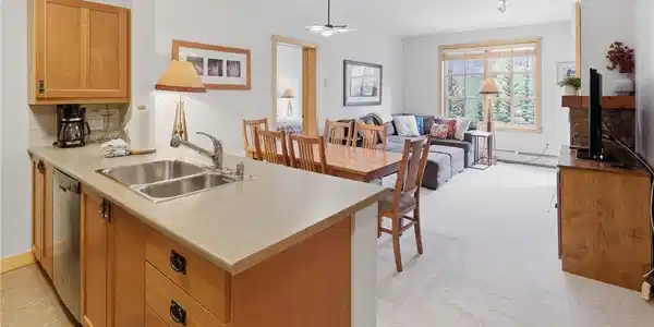 Image 2: Open-concept living space with a kitchen peninsula featuring a double-basin stainless steel sink, wood cabinetry, and stainless steel appliances Image 2: Open-concept living space with a kitchen peninsula featuring a double-basin stainless steel sink, wood cabinetry, and stainless steel appliances