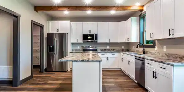 Image 3: Kitchen, Kitchen featuring wood-finish flooring, white cabinetry with dark hardware, a center island with a wood-clad base and stone countertop, and exposed wood ceiling beams