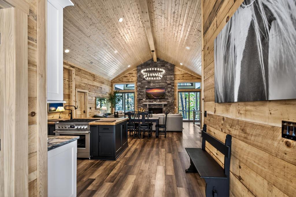 Image 4: Open-concept kitchen and dining area showcasing vaulted wood-finish ceilings, a central black island with seating, stainless steel appliances, and a brick fireplace