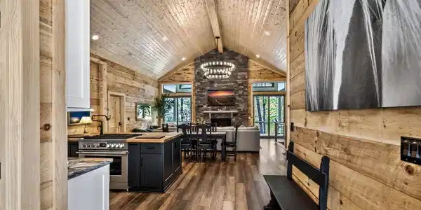 Image 4: Open-concept kitchen and dining area showcasing vaulted wood-finish ceilings, a central black island with seating, stainless steel appliances, and a brick fireplace