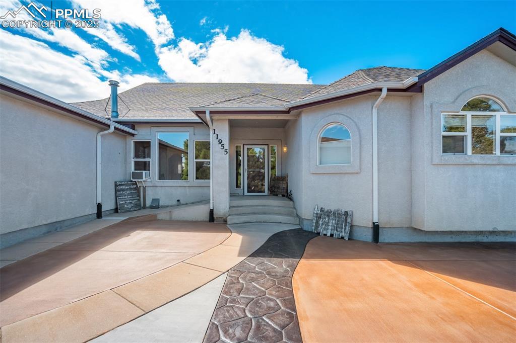 Image 4: Doorway to property featuring stucco siding and a shingled roof
