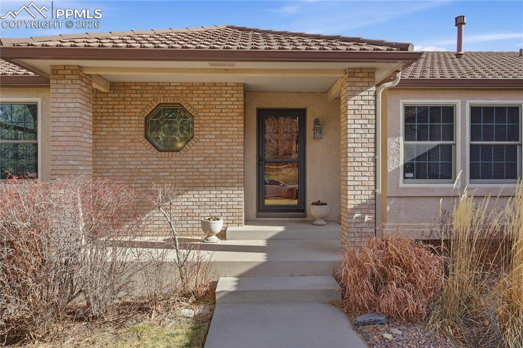 Image 4: Doorway to property featuring brick siding, a tile roof, and stucco siding