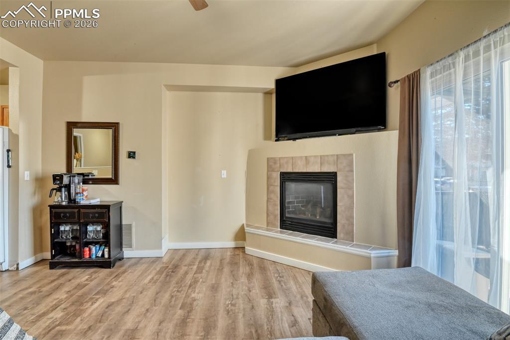 Image 4: Living area featuring a tile fireplace, ceiling fan, and light wood-type flooring