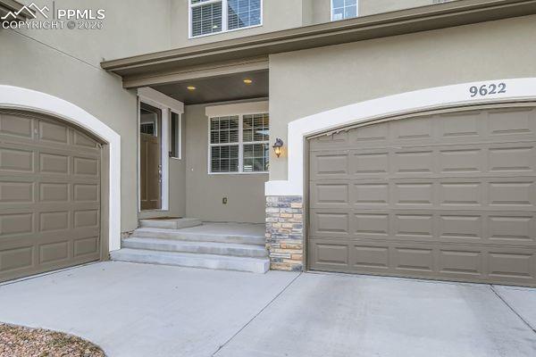 Image 3: View of exterior entry featuring stucco siding, stone siding, concrete driveway, and an attached garage
