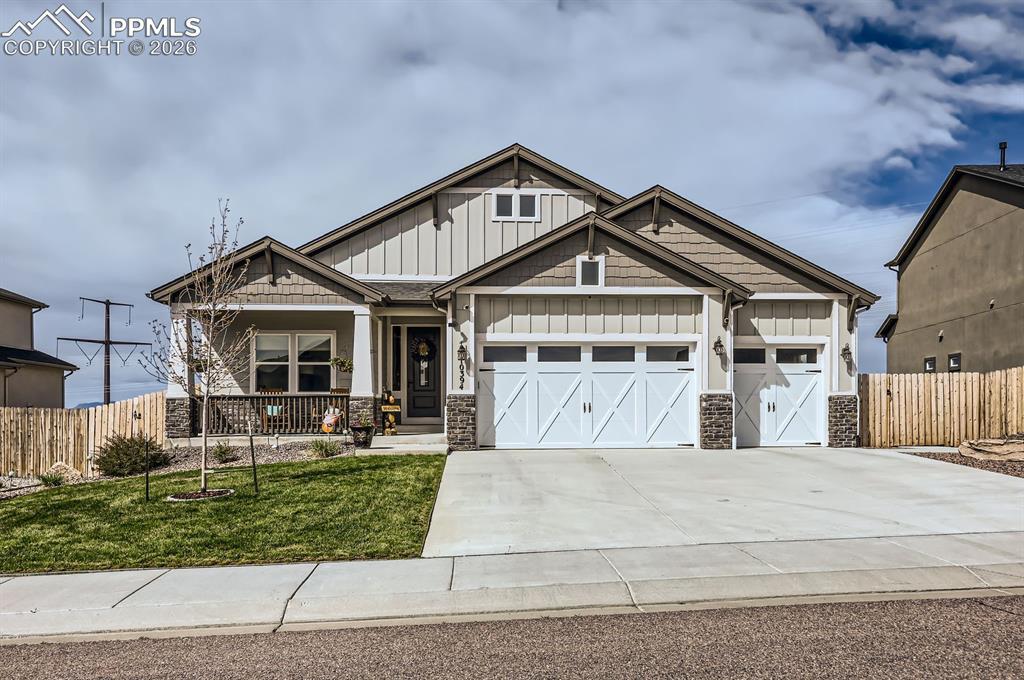 Image 1: Craftsman-style home featuring board and batten siding, stone siding, an attached garage, covered porch, and concrete driveway