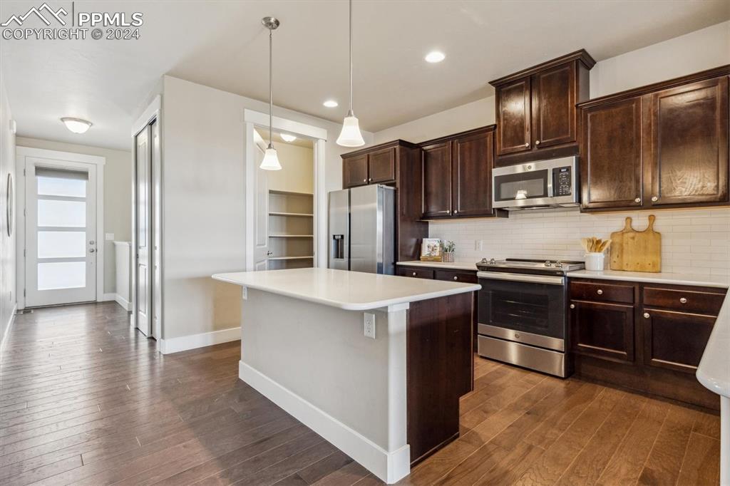 Image 4: Kitchen with decorative backsplash, stainless steel appliances, decorative light fixtures, dark hardwood / wood-style floors, and a kitchen island