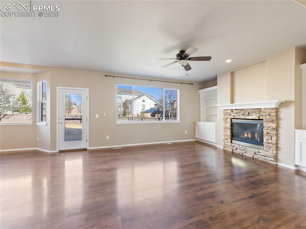 Image 3: Unfurnished living room with built in features, a ceiling fan, dark wood-type flooring, recessed lighting, and a stone fireplace