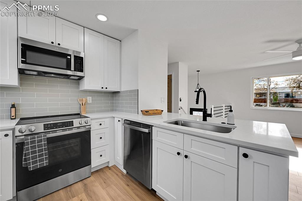 Image 2: Kitchen featuring appliances with stainless steel finishes, light wood-style flooring, white cabinets, light stone countertops, and recessed lighting