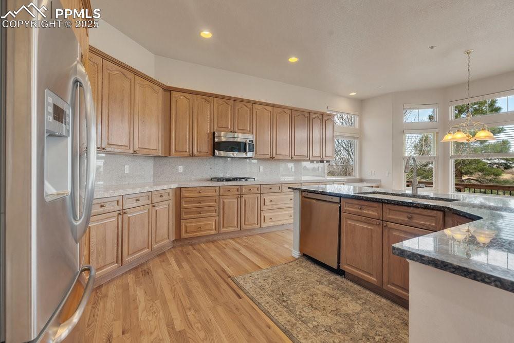 Image 2: Kitchen with appliances with stainless steel finishes, a sink, light wood finished floors, dark stone counters, and tasteful backsplash