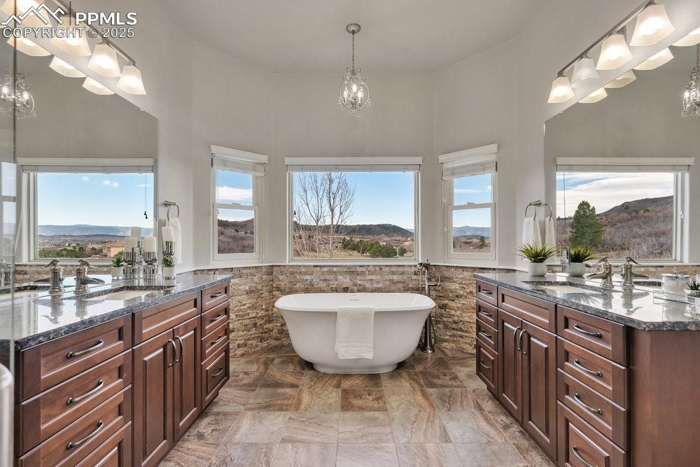 Image 4: Bathroom with a chandelier, vanity, a freestanding tub, wainscoting, and a towering ceiling
