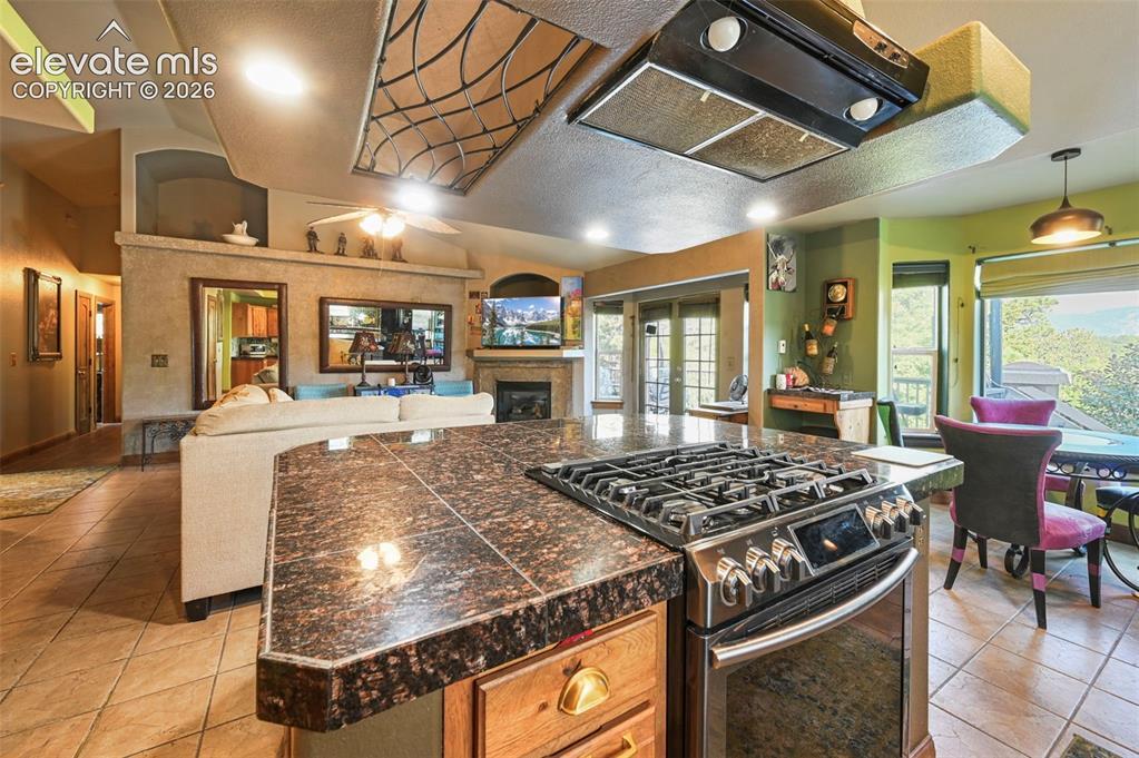 Image 2: Kitchen featuring a large central island with a dark stone countertop, an integrated cooktop, and an overhead lighting fixture