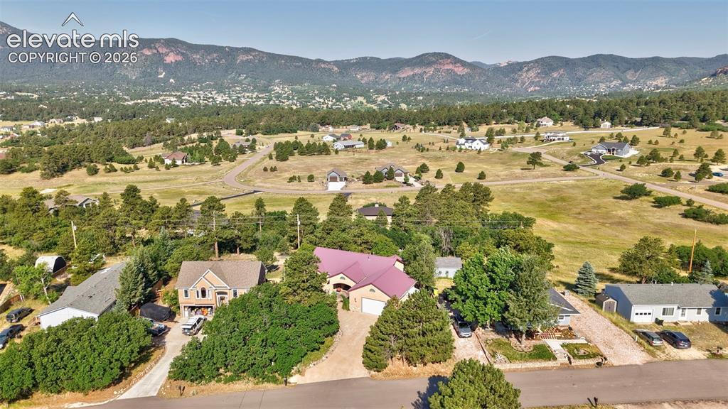 Image 3: Expansive property featuring a residence with a crimson roof, multiple mature trees, and a gravel driveway