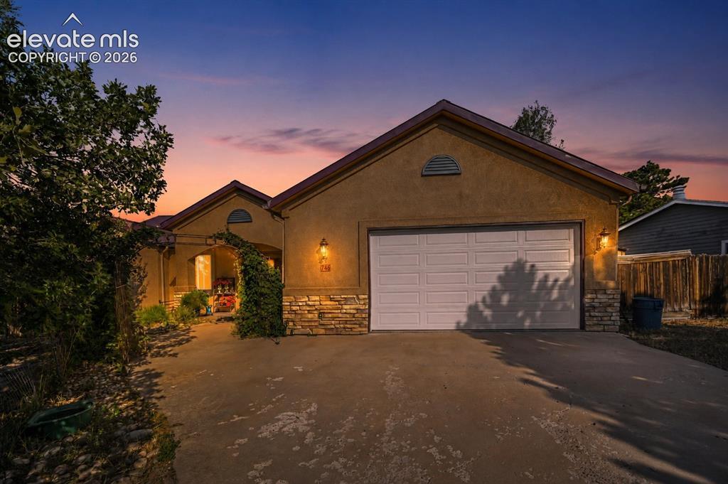 Image 4: Stucco exterior featuring a two-car garage, stone veneer accents, an arched entryway with climbing greenery, and a concrete driveway