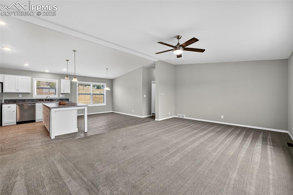 Image 4: Kitchen with dark countertops, hanging light fixtures, open floor plan, light carpet, and a kitchen island