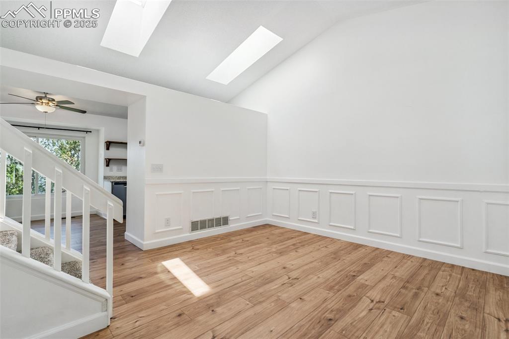 Image 3: Spare room featuring a skylight, light wood finished floors, stairs, lofted ceiling, and a wainscoted wall
