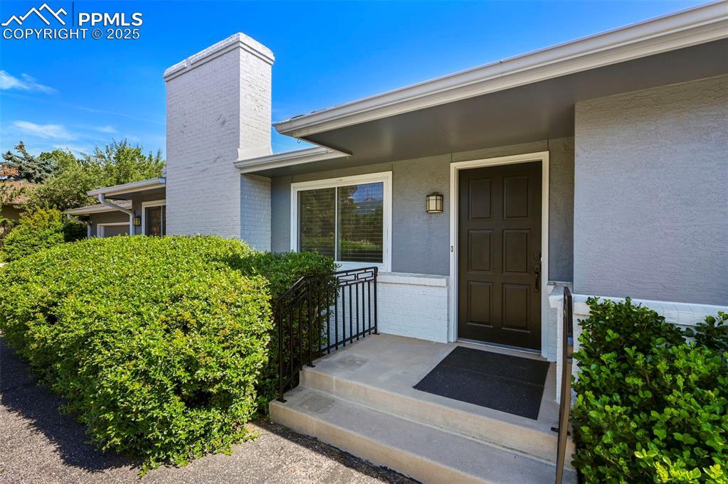 Image 3: Property entrance featuring a chimney, stucco siding, and brick siding