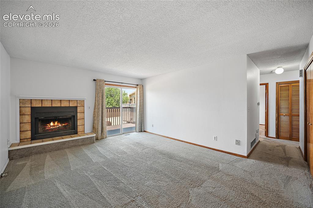 Image 4: Living area featuring a tiled fireplace, light-toned carpeting, and white walls