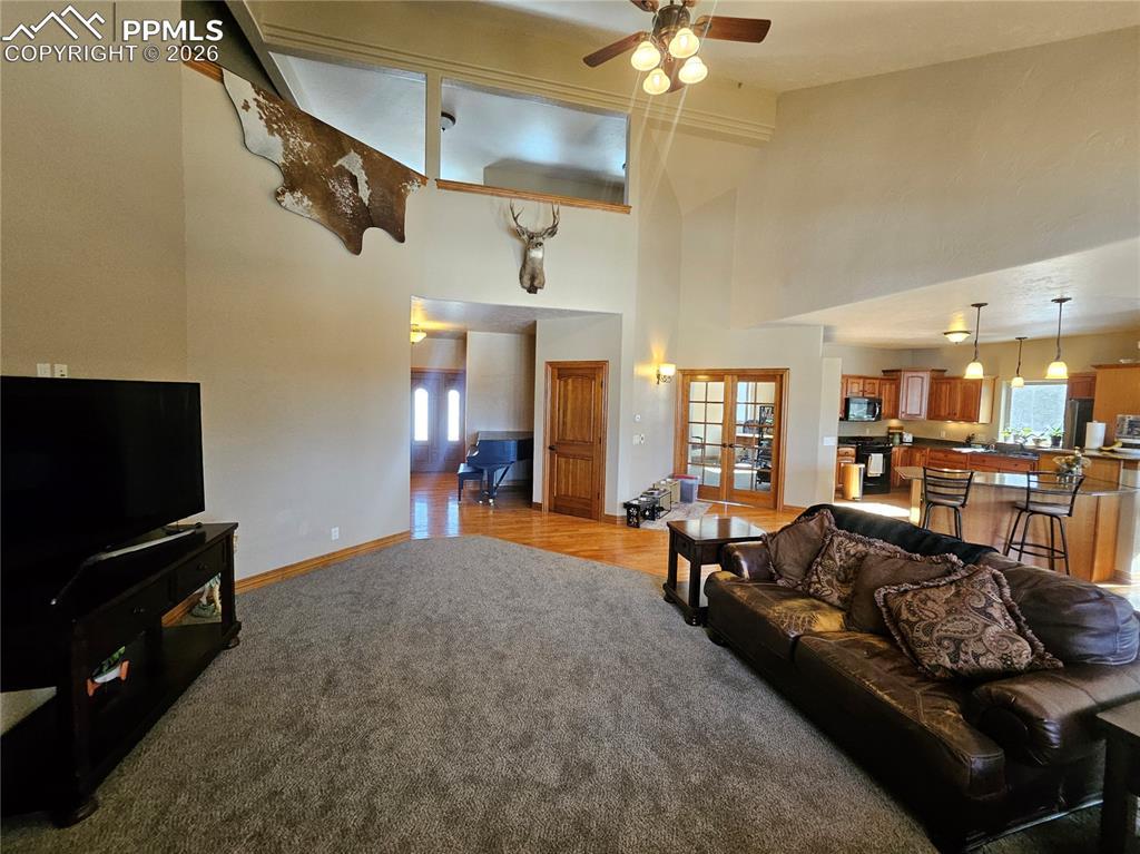 Image 4: Living area with French doors, light colored carpet, ceiling fan, plenty of natural light, and a high ceiling