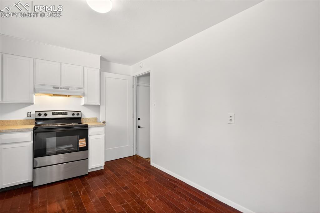 Image 4: Kitchen with stainless steel electric range, under cabinet range hood, dark wood-style floors, light countertops, and white cabinetry