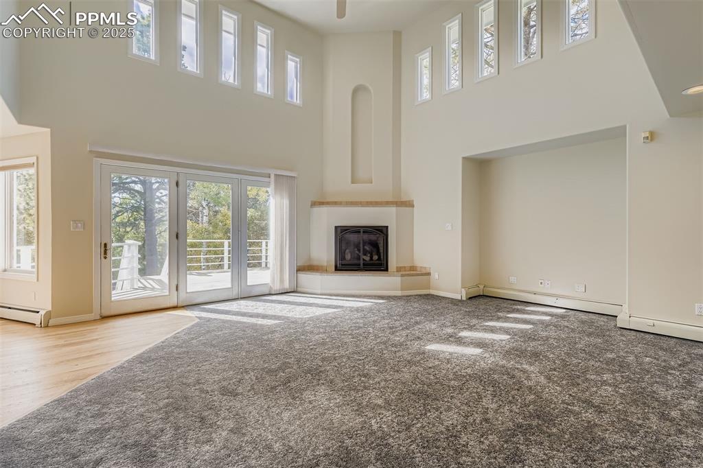 Image 4: Unfurnished living room featuring a high ceiling, plenty of natural light, a glass covered fireplace (gas), carpet, and baseboard heating (main flor)