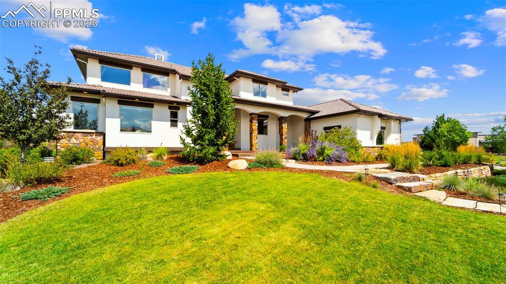 Image 3: Mediterranean / spanish-style home with stucco siding, stone siding, a front lawn, and covered porch