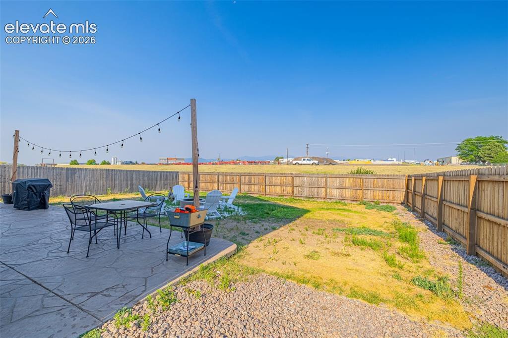 Image 2: Expansive backyard featuring a concrete patio with string lighting, a gravel border, and a wooden privacy fence