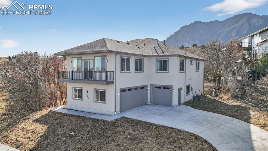 Image 3: Back of property featuring a balcony, a garage, stucco siding, a mountain view, and driveway