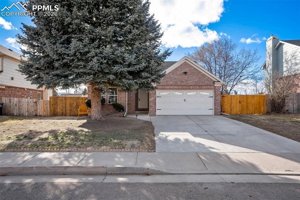 Image 1: View of property hidden behind natural elements with brick siding, a garage, and driveway