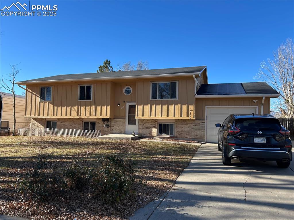 Image 1: Split foyer home featuring concrete driveway, an attached garage, brick siding, and board and batten siding