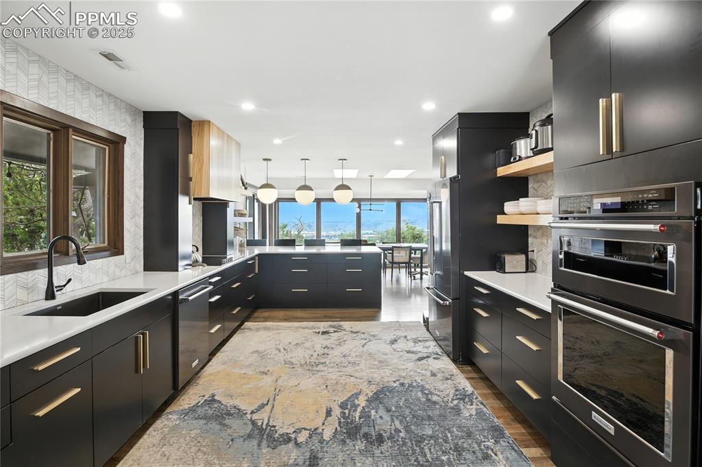 Image 4: Kitchen featuring dark cabinetry, modern cabinets, appliances with stainless steel finishes, decorative light fixtures, and recessed lighting