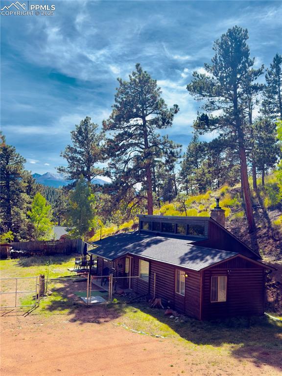 Image 1: View of home's exterior with a gate, log veneer siding, a chimney, and view of wooded area