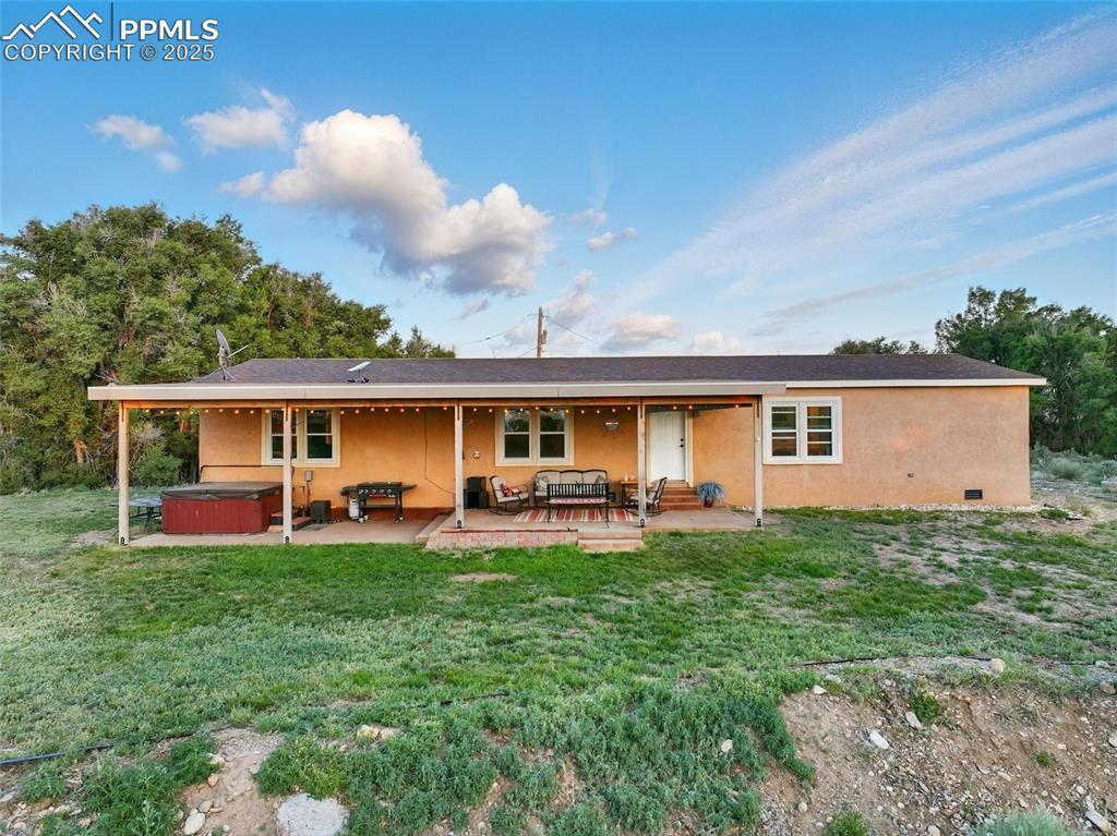 Image 4: Rear view of property featuring a hot tub, a patio, stucco siding, and a yard