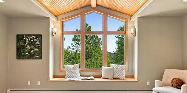 Image 2: Primary bedroom on the entry level with vaulted wood ceilings, intentional lighting, treetop views and serenity.