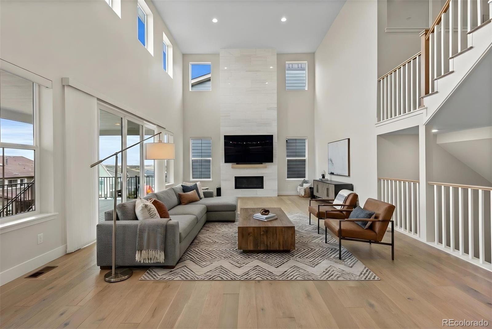 Image 4: Bathed in natural light from soaring windows, the great room impresses with dramatic ceiling heights, a sleek fireplace focal point, and seamless access to the covered deck for elevated indoor-outdoor living. *This photo has been virtually staged. Image 4: Bathed in natural light from soaring windows, the great room impresses with dramatic ceiling heights, a sleek fireplace focal point, and seamless access to the covered deck for elevated indoor-outdoor living. *This photo has been virtually staged.