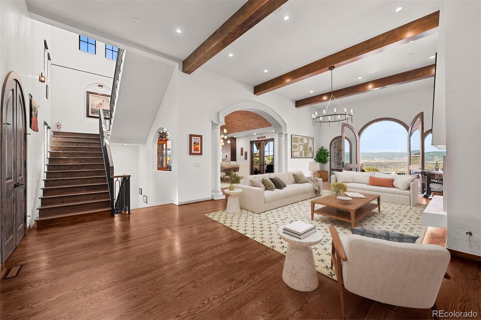 Image 4: Beautiful great room with soaring ceilings, exposed beams, and arched doors opening to mountain view. The open layout flows seamlessly into the kitchen and dining areas - virtually staged. Image 4: Beautiful great room with soaring ceilings, exposed beams, and arched doors opening to mountain view. The open layout flows seamlessly into the kitchen and dining areas - virtually staged.