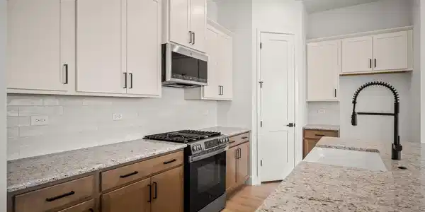 Image 4: Modern kitchen featuring light-toned upper cabinetry and wood-finish lower cabinetry, complemented by a granite speckled countertop. Image 4: Modern kitchen featuring light-toned upper cabinetry and wood-finish lower cabinetry, complemented by a granite speckled countertop.