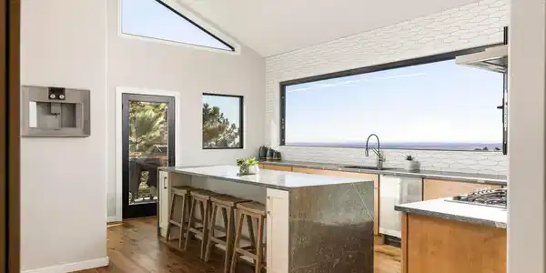 Image 4: The kitchen is anchored by a dramatic waterfall island, Gaggenau appliances, custom cabinetry, and seamless access to the outdoor living spaces. Image 4: The kitchen is anchored by a dramatic waterfall island, Gaggenau appliances, custom cabinetry, and seamless access to the outdoor living spaces.