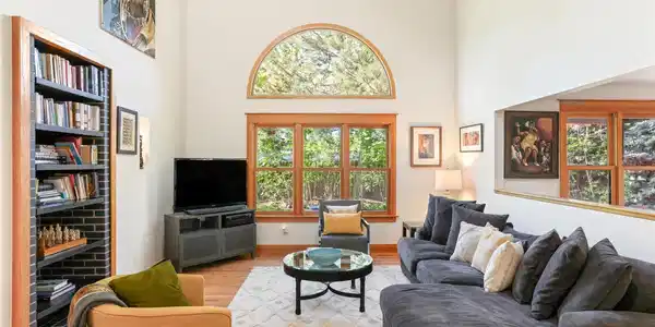 Image 4: The main level living room offers a double-height vaulted ceiling and large picture windows with private, treed views to the back yard and garden. Image 4: The main level living room offers a double-height vaulted ceiling and large picture windows with private, treed views to the back yard and garden.