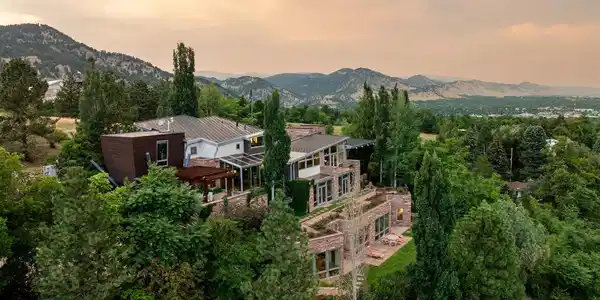 Image 3: The main house at dusk, set into the wooded hillside with the foothills and Boulder valley beyond. Image 3: The main house at dusk, set into the wooded hillside with the foothills and Boulder valley beyond.