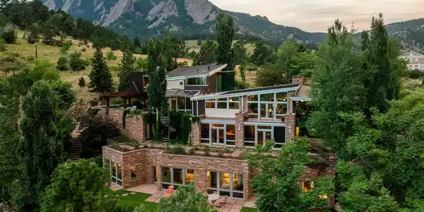 Image 4: The main house at dusk below the Flatirons, its stone terraces glowing above the meadow, with the historic Chautauqua Auditorium just beyond. Image 4: The main house at dusk below the Flatirons, its stone terraces glowing above the meadow, with the historic Chautauqua Auditorium just beyond.